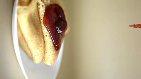 A stack of thin golden pancakes on a white platter, drizzled with sweet jam Stock Footage 305072631