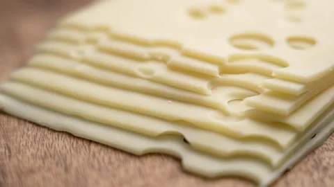 Stack of thin Swiss cheese slices with round holes on a wooden surface Stock Footage 303854143
