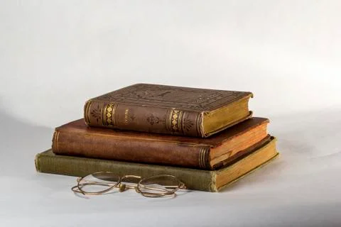 Stack of Three Antique books with a pair of vintage eyeglasses on a white bac Stock Photos