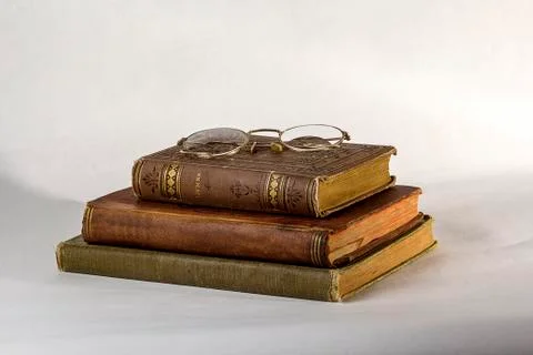 Stack of Three Antique books with a pair of vintage eyeglasses on a white bac Stock Photos