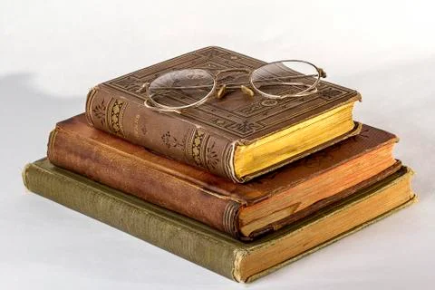 Stack of Three Antique books with a pair of vintage eyeglasses on a white bac Stock Photos