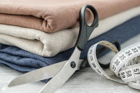 Stack of three knitted fabrics, scissors of dressmaker and measuring tape. Stock Photos