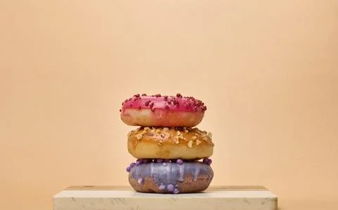 Stack of three multicolored donuts with glaze and sprinkles on a board Stock Photos