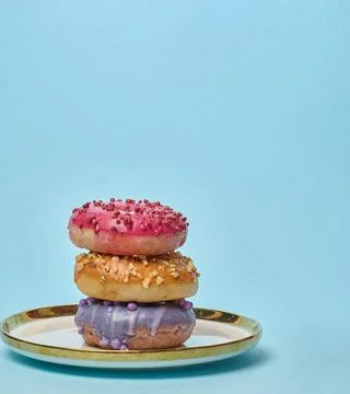 Stack of three multicolored donuts with glaze and sprinkles on a white plat.. Stock Photos