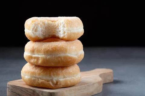 Stack of three ring donuts on a wooden board with a top bite Stock Photos
