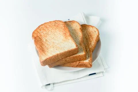 Stack of toast on white plate and white placemat on white background, top vie Stock Photos