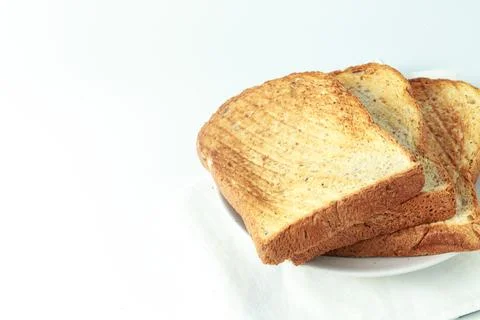 Stack of toast on white plate and white placemat on white background, top vie Stock Photos