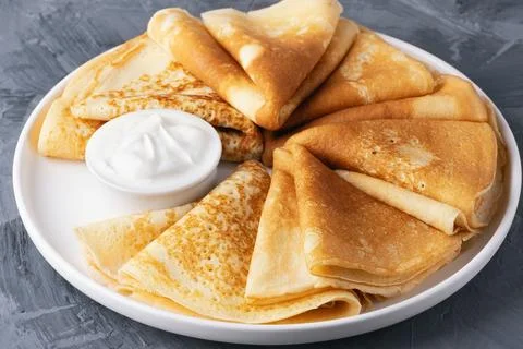 Stack of traditional russian pancakes blini with sour cream on gray backgroun Stock Photos