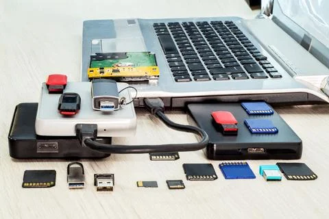 Stack of USB flash drives, memory cards, external hard drives in front, lapto Stock Photos
