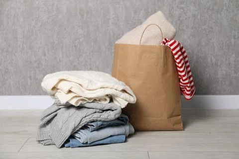 Stack of used clothes and paper bag on floor near grey wall 스톡 사진
