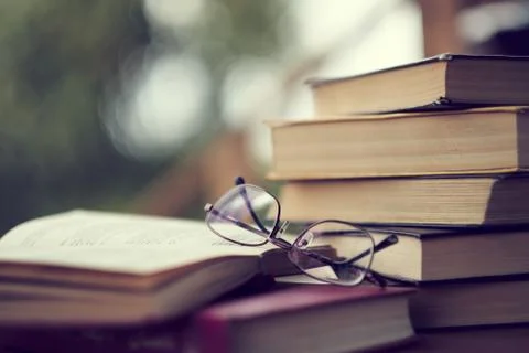 Stack of vintage books on the table, glasses and an open book. in the background Foto stock