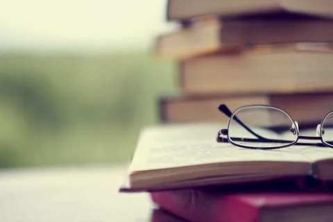 Stack of vintage books on the table, glasses and an open book. in the background 库存照片