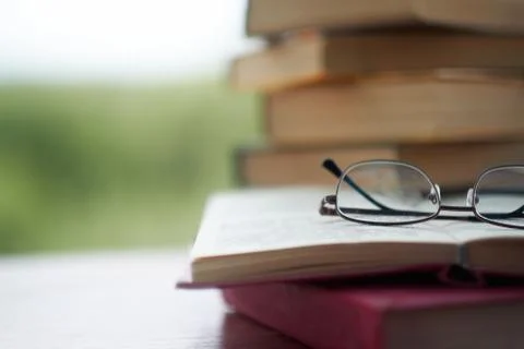 Stack of vintage books on the table, glasses and an open book. in the background Foto stock