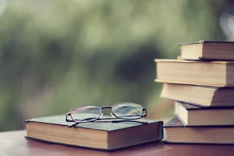 Stack of vintage books on the table, glasses and an open book. in the background 库存照片