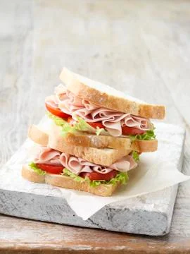 Stack of wafer thin ham sandwiches on sliced white bread with salad leaves and Stock Photos