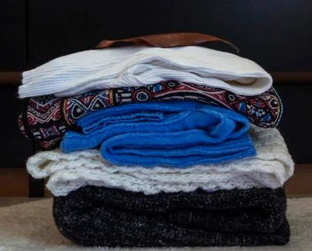 A stack of warm clothes is folded near the dresser Stock Photos