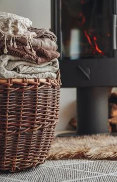 A stack of warm clothes in a wicker basket an iron fireplace wit Stock Photos