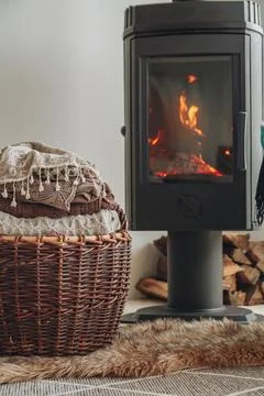 A stack of warm clothes in a wicker basket an iron fireplace wit Stock Photos