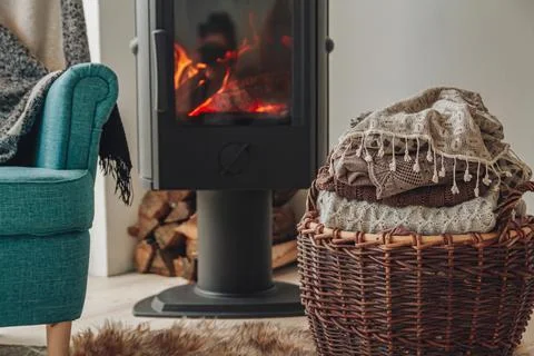 A stack of warm clothes in a wicker basket an iron fireplace wit Stock Photos