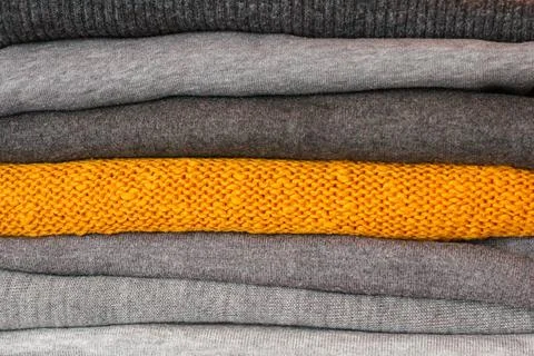 A stack of warm, cozy clothes for winter. among the gray sweaters, one is yel Photos