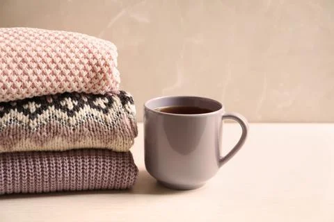 Stack of warm knitted clothes and cup of tea on table 스톡 사진