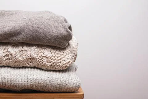 Stack of warm knitted woolen sweaters against white wall Foto stock