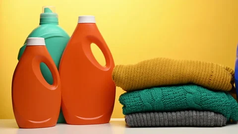 Stack of washed folded clothes and plastic orange large bottles with liquid dete Stock Footage 165952741