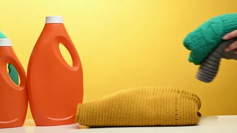 Stack of washed folded clothes and plastic orange large bottles with liquid dete Stock Footage 240096899