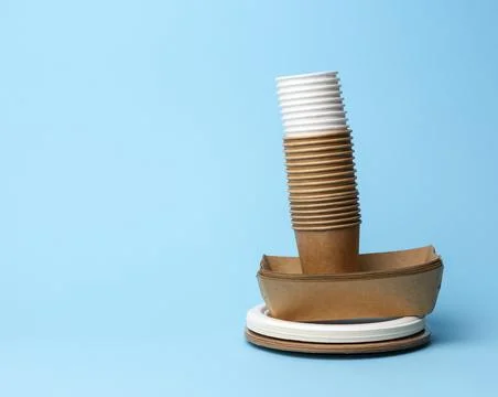 Stack of white and brown paper cups and round plates on a blue background Stockfoto's