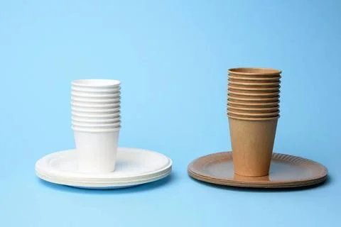 Stack of white and brown paper cups and round plates on a blue background ... Stock Photos