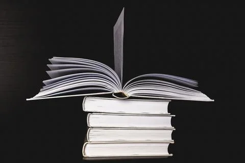 A stack of white blank books on a shelf on a black background, the top book i Stock Photos