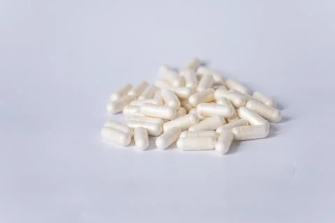 A stack of white capsules is scattered on a white background - medicines or Stock Photos