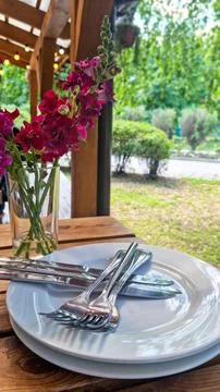 Stack of white ceramic plates with metal forks and knives on wooden table Stock Photos