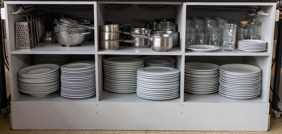Stack white clean plates and other metal utensils  on the shelves in commerci 스톡 사진
