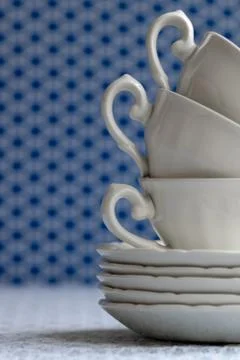 Stack of white cups and dishes on a white lace tablecloth. Stock Photos