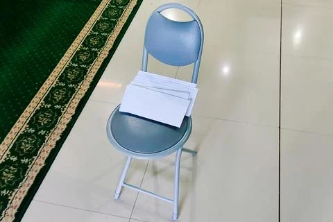 A stack of white envelopes placed on a gray folding chair inside a mosque, .. Foto stock