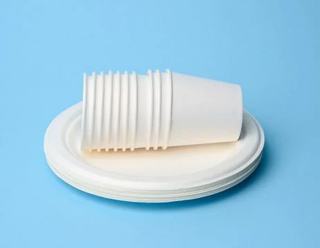 Stack of white paper cups and round plates on a blue background Stock Photos