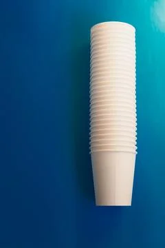 A stack of white paper cups lies on a blue background, disposable cups on a b Stock Photos