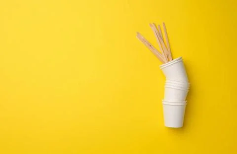 Stack of white paper cups on a yellow background. Plastic rejection concep... 库存照片