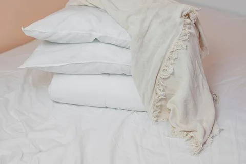 Stack of white pillows and blankets lies on the bed on a white sheet on top Stock Photos