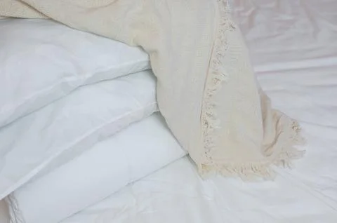 Stack of white pillows and blankets lies on the bed on a white sheet on top Stock Photos