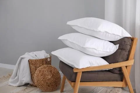 Stack of white pillows, armchair and wicker basket on floor indoors Foto stock