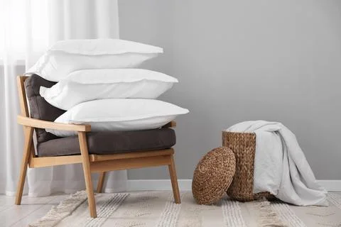 Stack of white pillows, armchair and wicker basket on floor indoors 写真素材