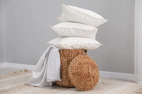 Stack of white pillows, blanket and wicker basket on floor indoors Foto stock
