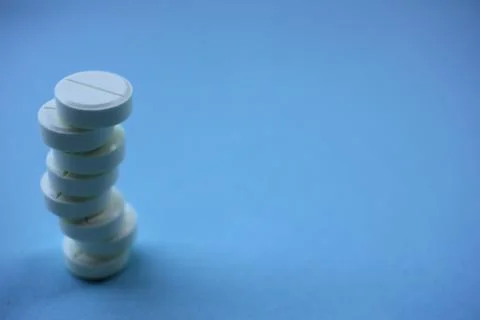 Stack of white pills on blue background with copy space. Stock Photos