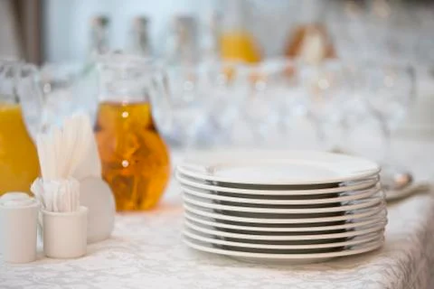 A stack of white plates on the table with a carafe of juice plastic cups Stock Photos
