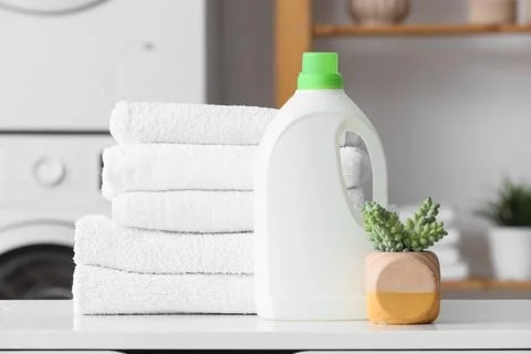 Stack of white towels with laundry detergent on shelf in room Stock Photos