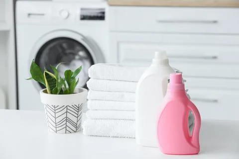 Stack of white towels with laundry detergents and plant on table in room Stock Photos
