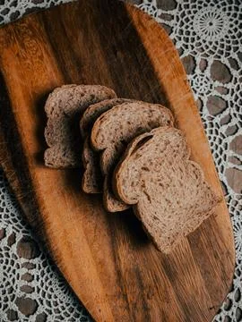 Stack of Wholegrain Bread Slices on Rustic Wooden Board with Lace Tablecloth Фото