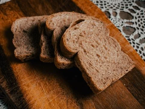 Stack of Wholegrain Bread Slices on Rustic Wooden Board with Lace Tablecloth Stock Photos